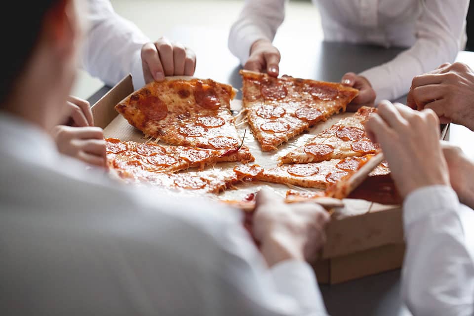 Article featured image showing business people sharing a pizza metaphorically referring to community shared moments